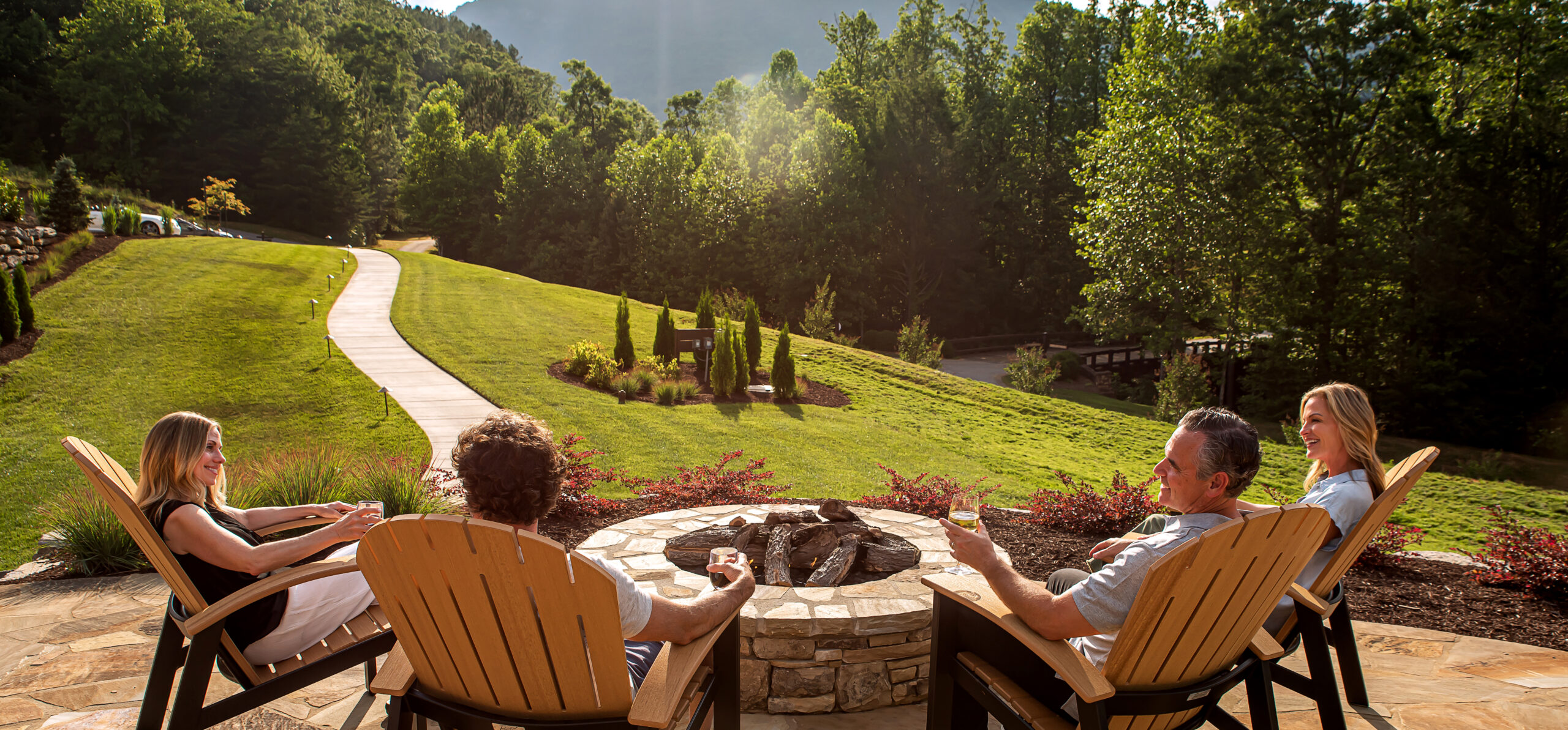 group of four adults enjoy drinks by firepit