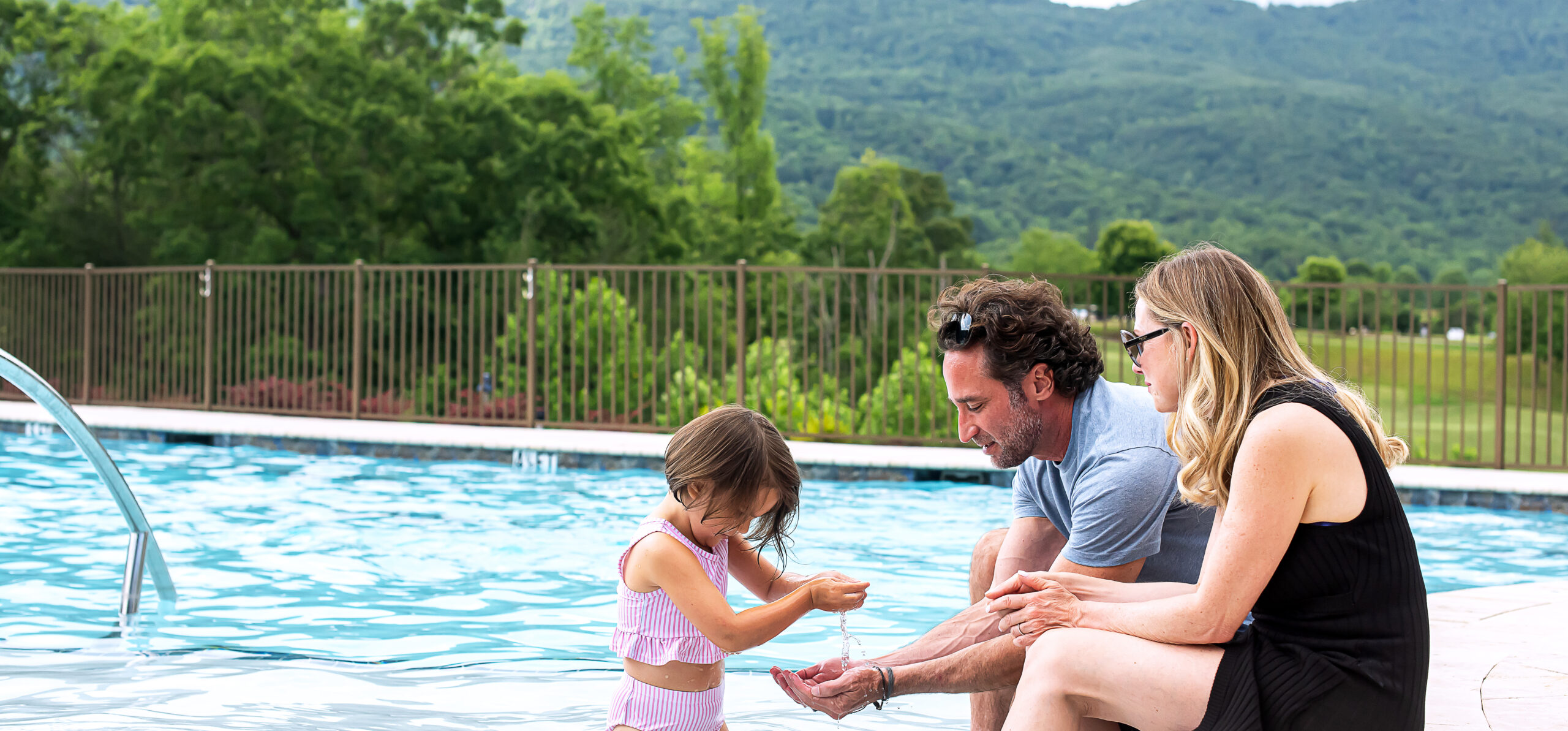 parents play with toddler daughter beside pool