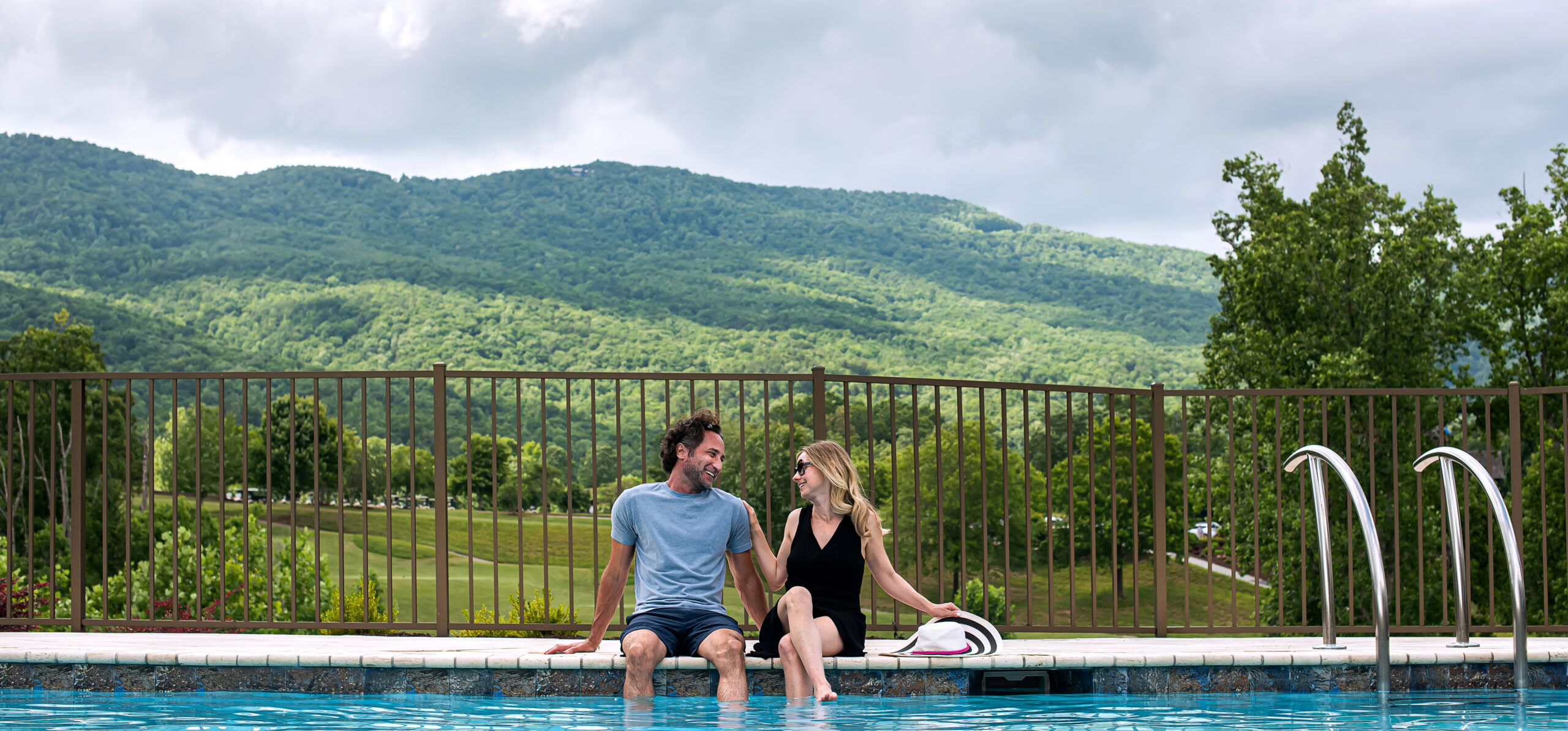 couple with feet in pool smile at each other